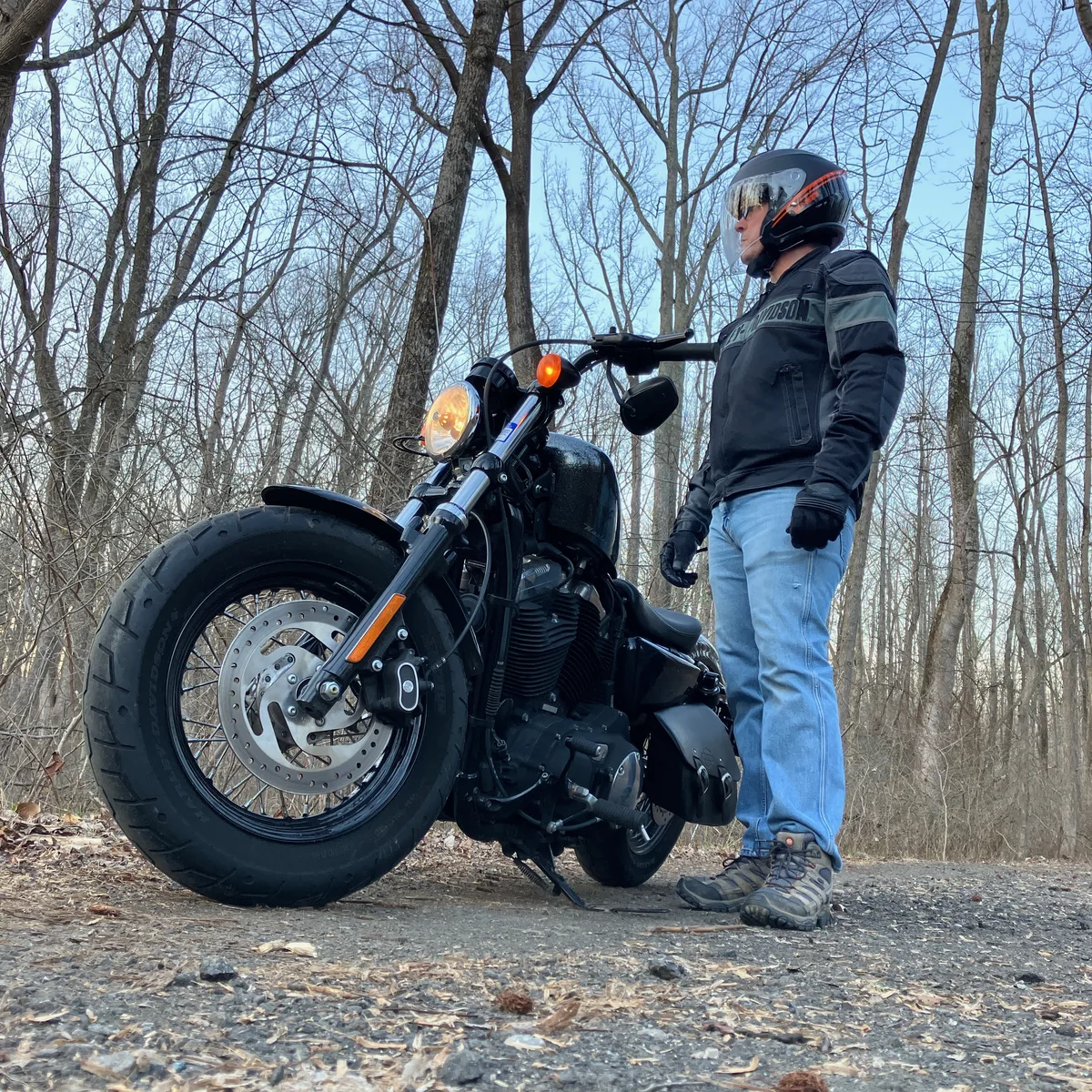 Thad in riding gear next to his motorcycle on a wooded gravel path in the evening.