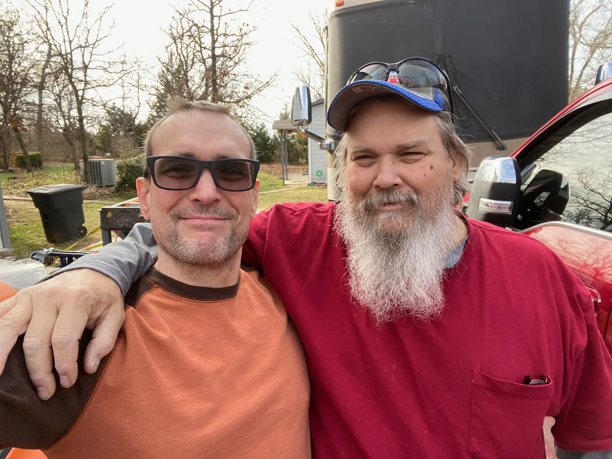 Thad with his arm around his brother Bill, both smiling outdoors.