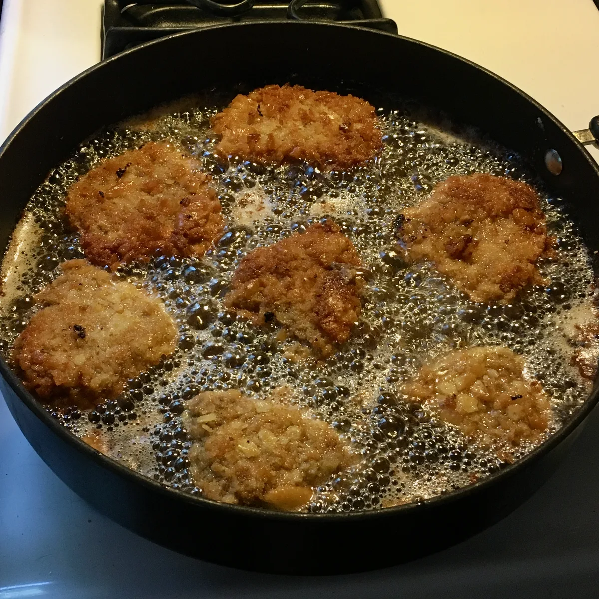 Several pieces of country fried steak cooking in hot oil in a skillet, coated with crushed Ritz crackers.