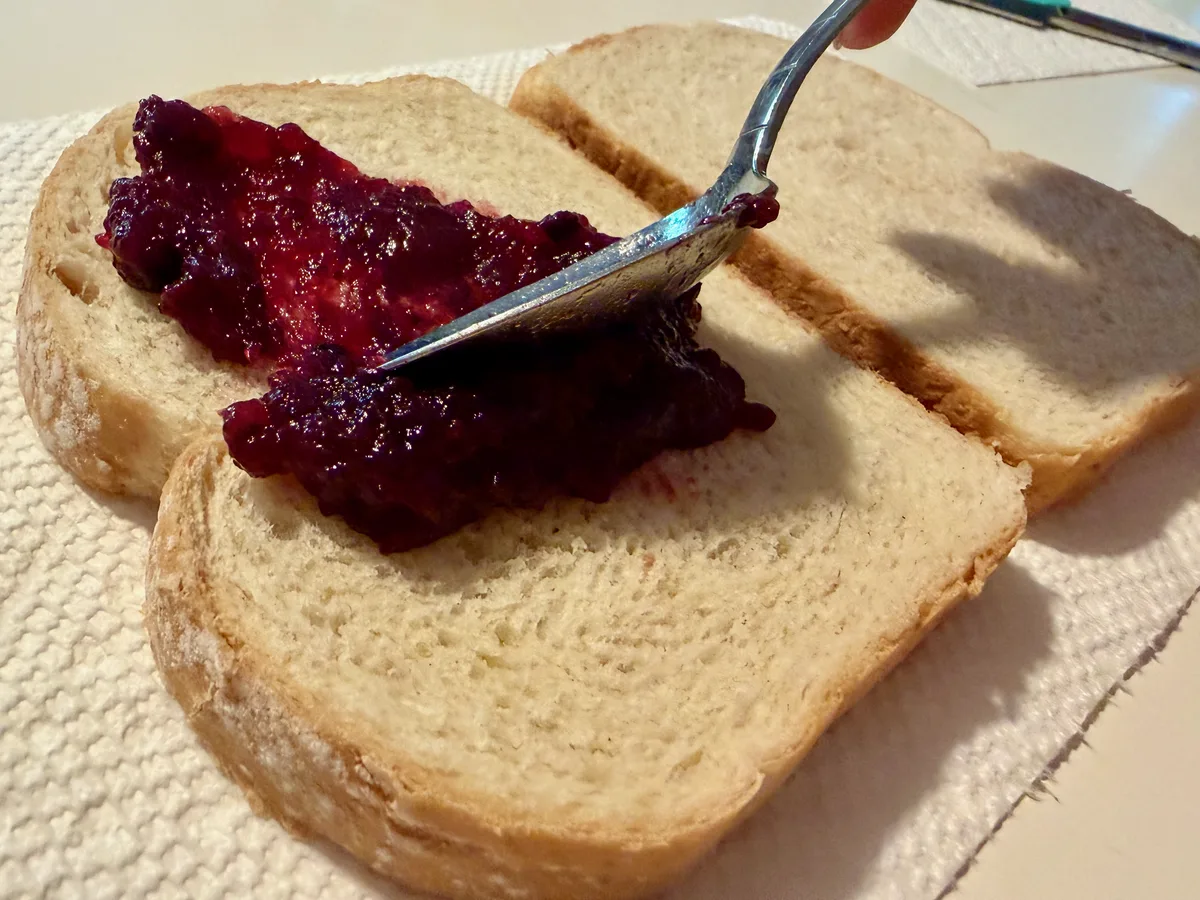 Berry jam being spread over bread with the back of a spoon.