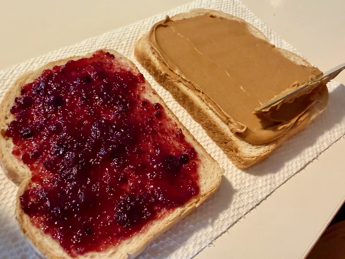 A slice of bread fully covered in peanut butter next to a jam covered slice.