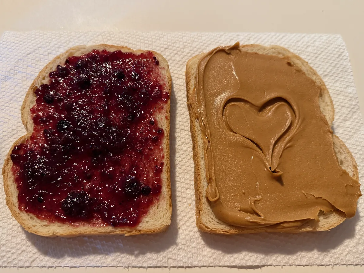 Jam and peanut butter slices side by side, a heart shape traced into the peanut butter.
