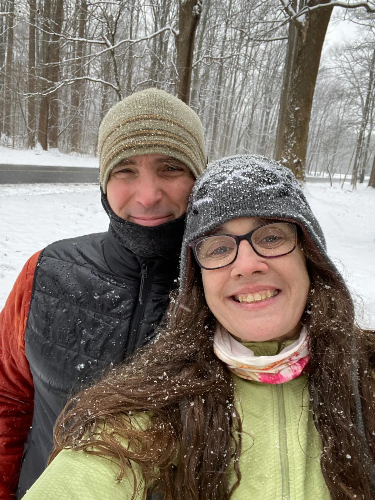 Thad and Jolynn smiling in a snowy wooded area, snowflakes visible on their clothing.