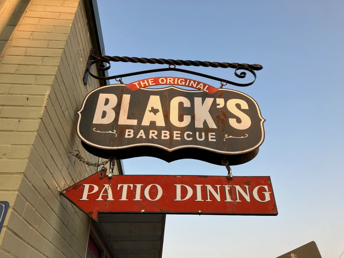Black's Barbecue sign hanging outside the restaurant in Texas, pointing to patio dining.