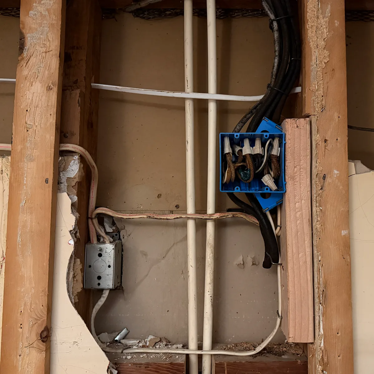 Updated electrical wiring in an open wall cavity, with wire nuts capped inside a blue junction box.