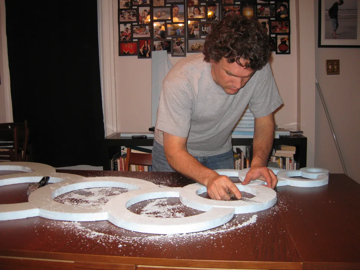 Thad shaping cut foam circles with a rasp file, foam dust scattered across the table.