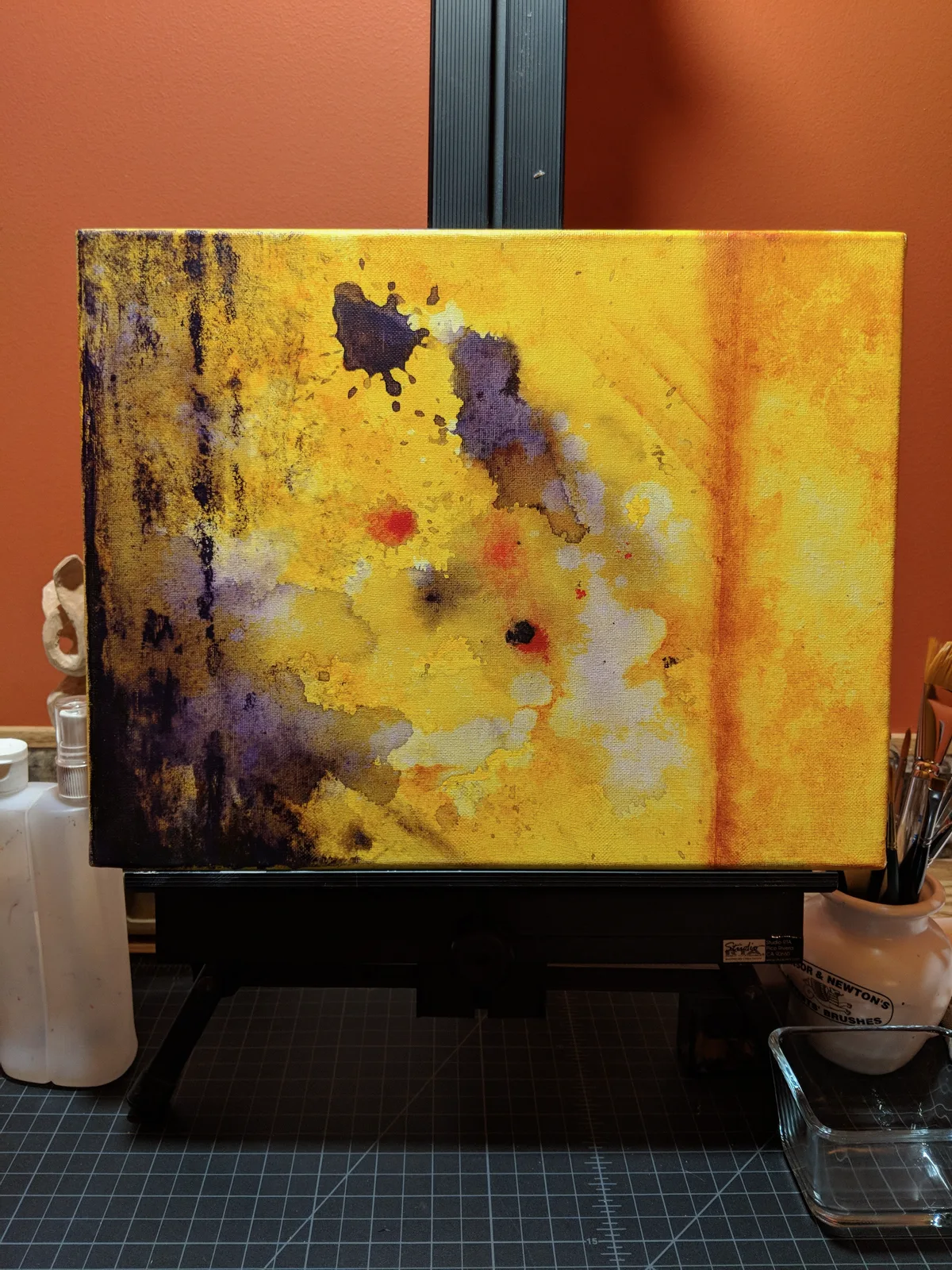 Abstract painting on an easel in yellow orange with purple accents