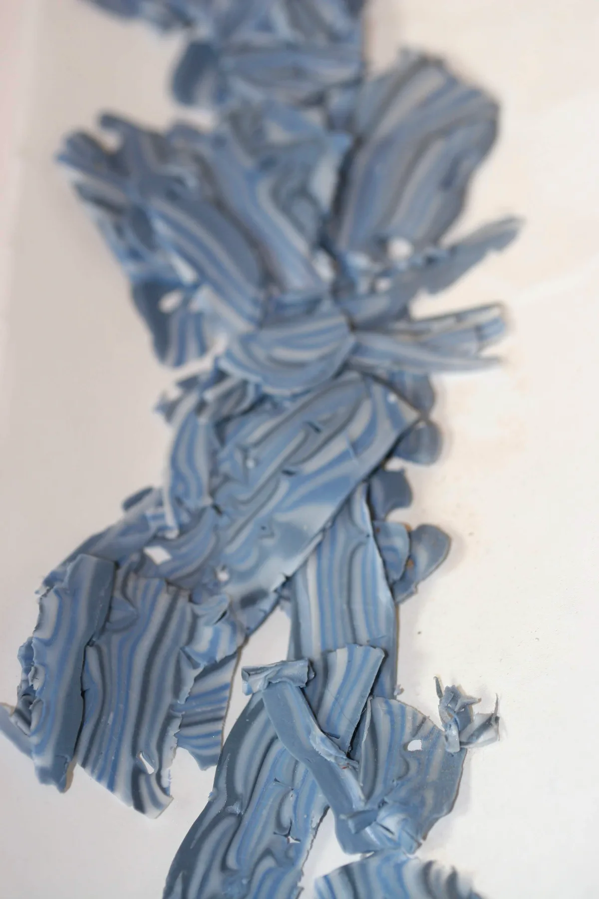 Layered and shaved polymer clay in blue and white marbled strips, ready to be shaped into balls.