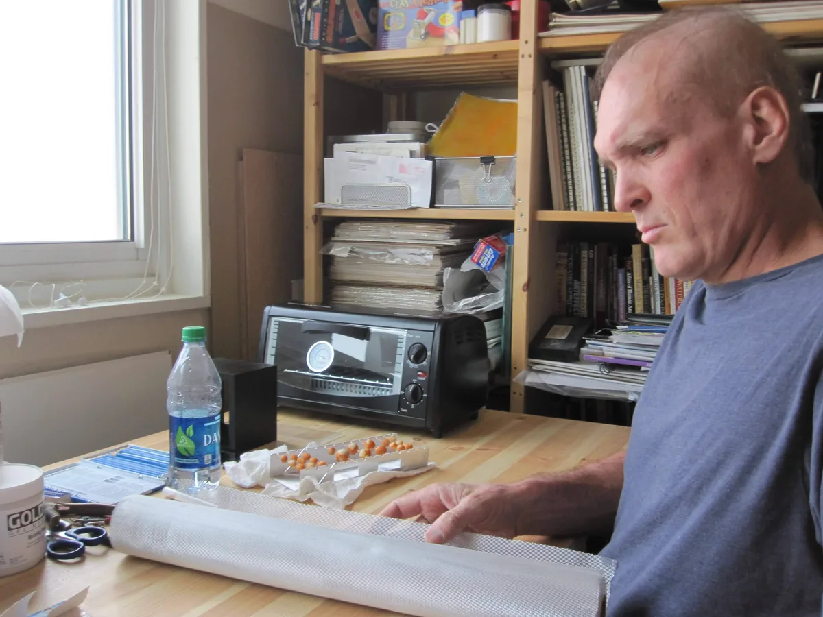Thad focused on unrolling wire mesh, showing signs of hair loss from chemotherapy treatment.