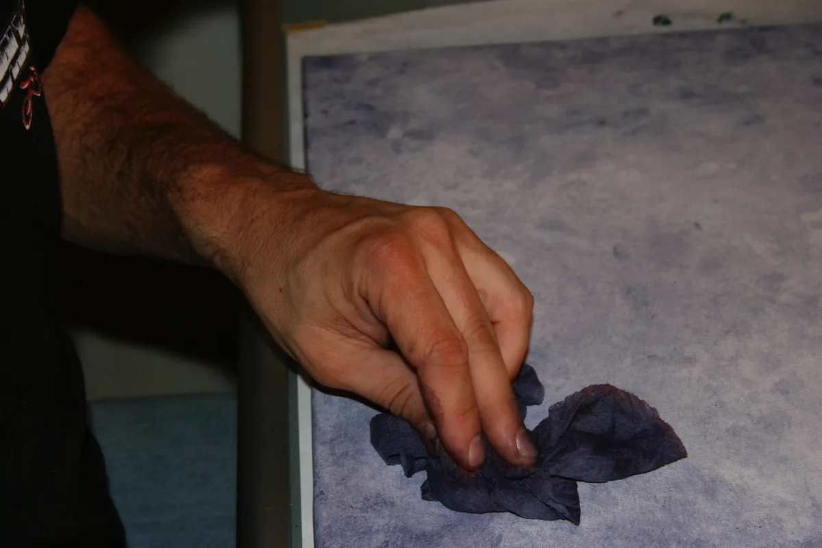 Close-up of a hand pressing a cloth into the wet textured canvas