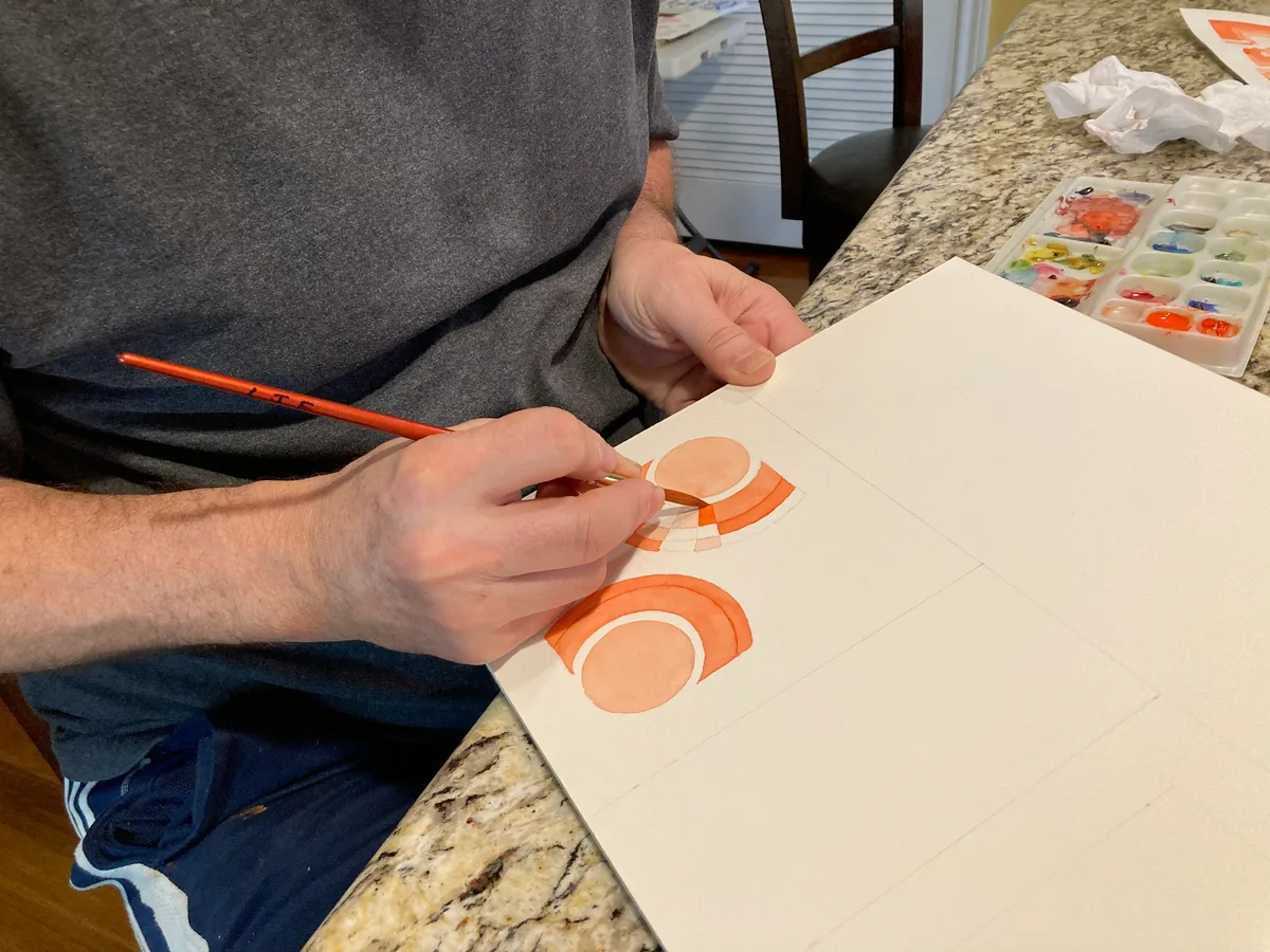 Thad painting a vermilion watercolor piece at the counter