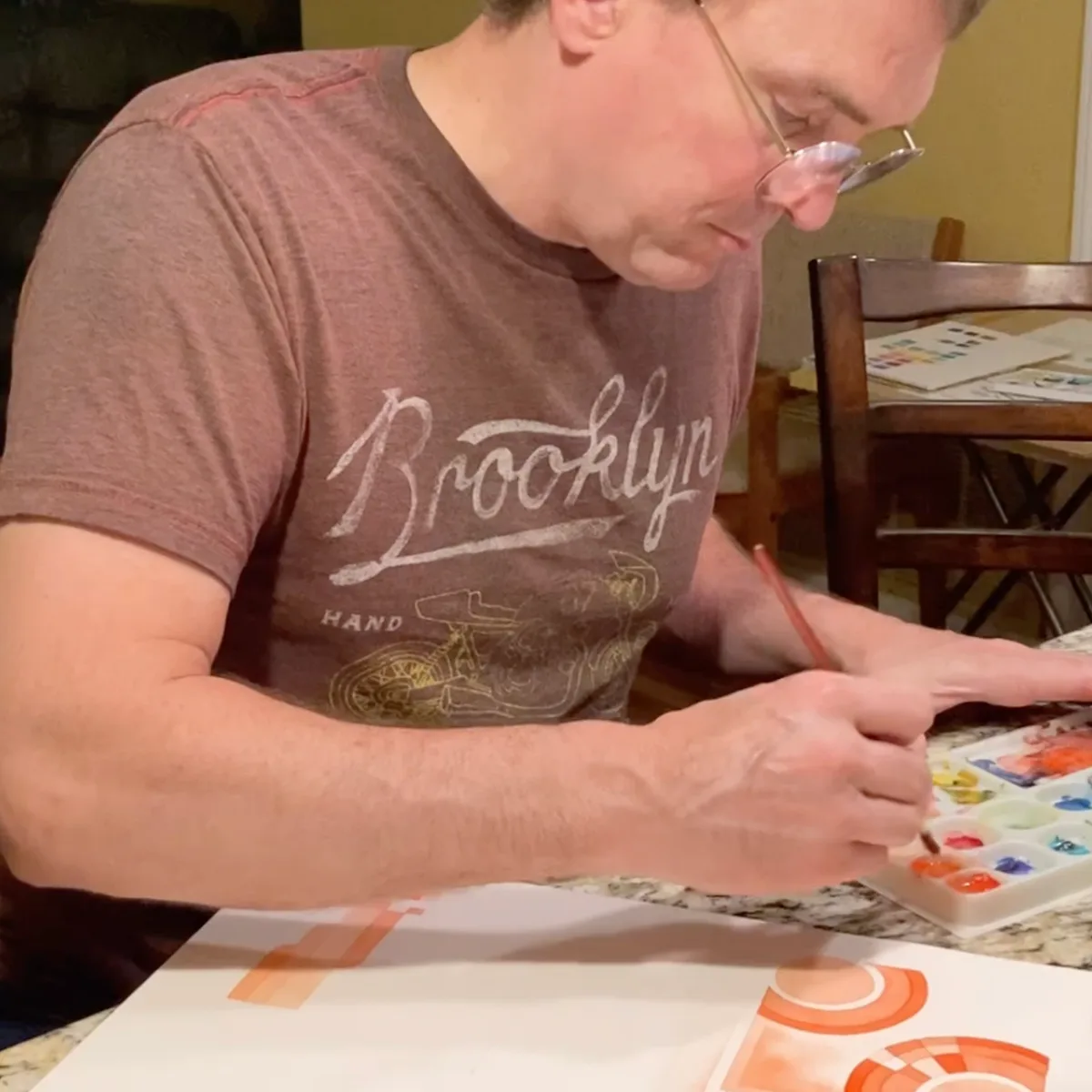 Thad painting a vermilion watercolor piece at the table