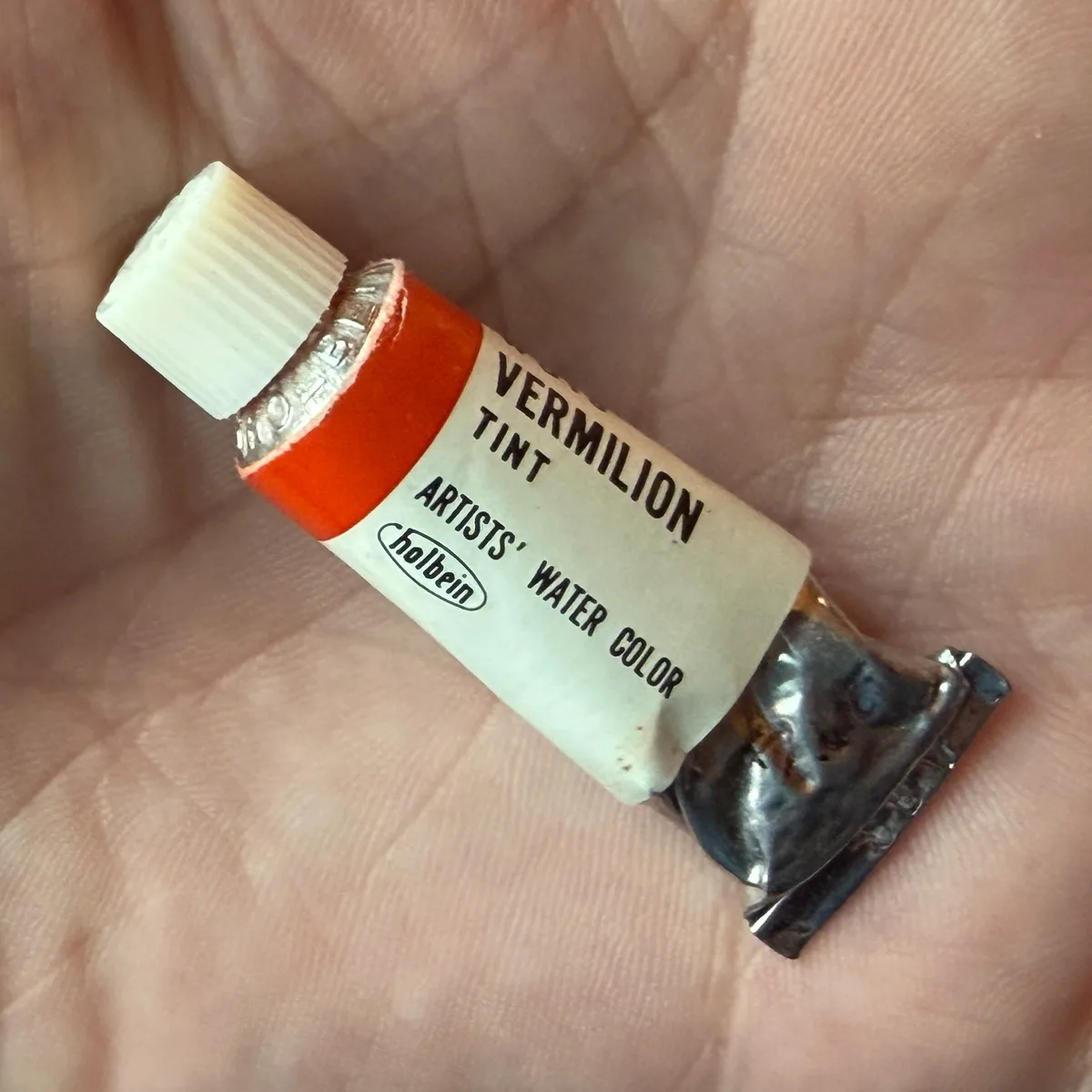 Tube of Holbein Vermilion Tint watercolor paint held in a hand